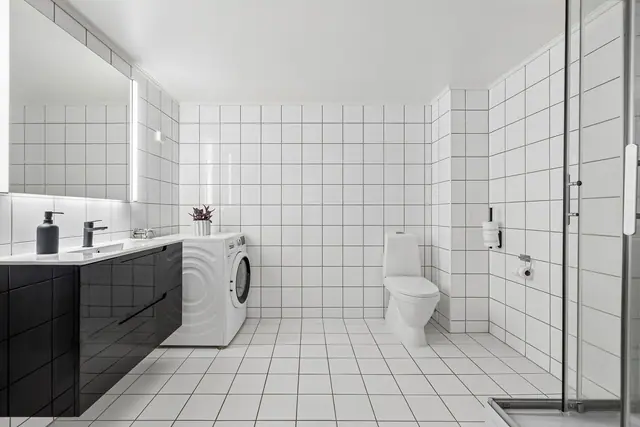 Baderommet er flislagt og har innredning med nedfelt servant, skap, toalett, dusjkabinett og opplegg for vaskemaskin.