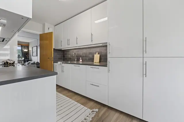 Kjøkken med moderne, hvite fronter og mørk laminat benkeplate.