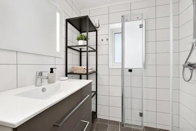 Stilrent bad med speil med belysning og dusj med glassdører.