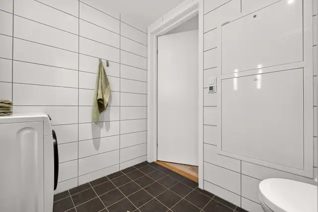 Praktisk utformet bad med flislagte overflater og opplegg for vaskemaskin.
